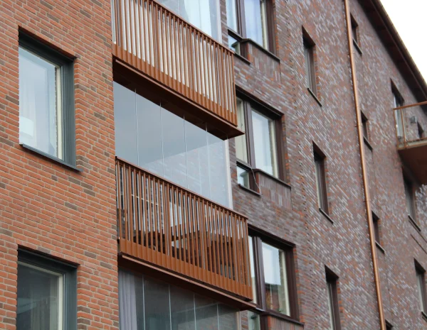balkonginglasning med brunt räcke på fastighet med tegelfasad